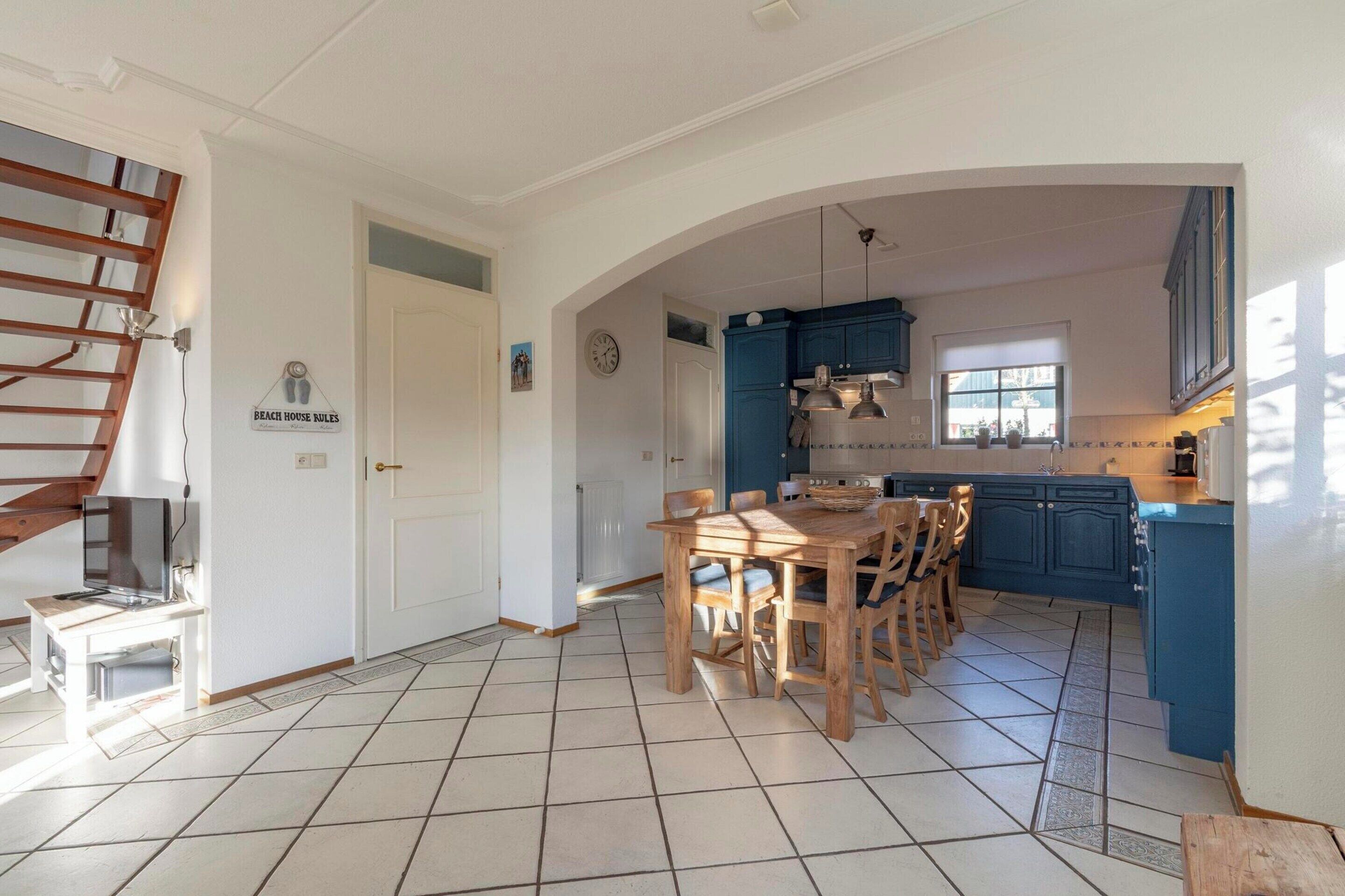 Une cuisine avec des meubles de rangement bleus, une table à manger en bois et un escalier.