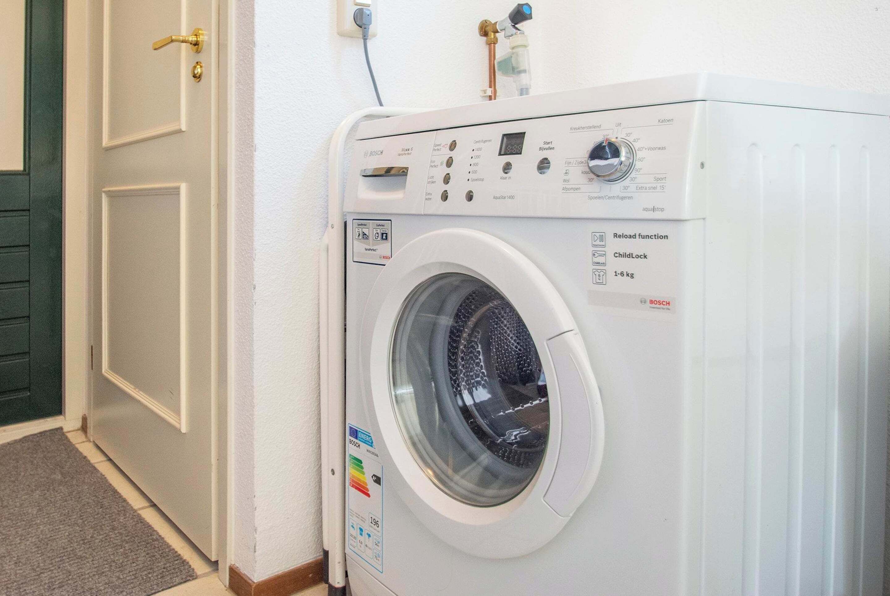 Una lavadora blanca Bosch en una habitación con una puerta cerrada y una alfombra gris.