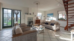 A spacious living room with wicker furniture, a fireplace, and a wooden staircase. - De Buitenplaats 7 Villa With Dune Views (Callantsoog)