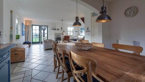 A spacious kitchen with a large wooden table and chairs, pendant lights, and a clock on the wall. - De Buitenplaats 7 Villa With Dune Views (Callantsoog)