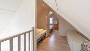 Une petite chambre mansardée, avec un plafond haut, un plancher en bois, un lit, une commode et une petite fenêtre.