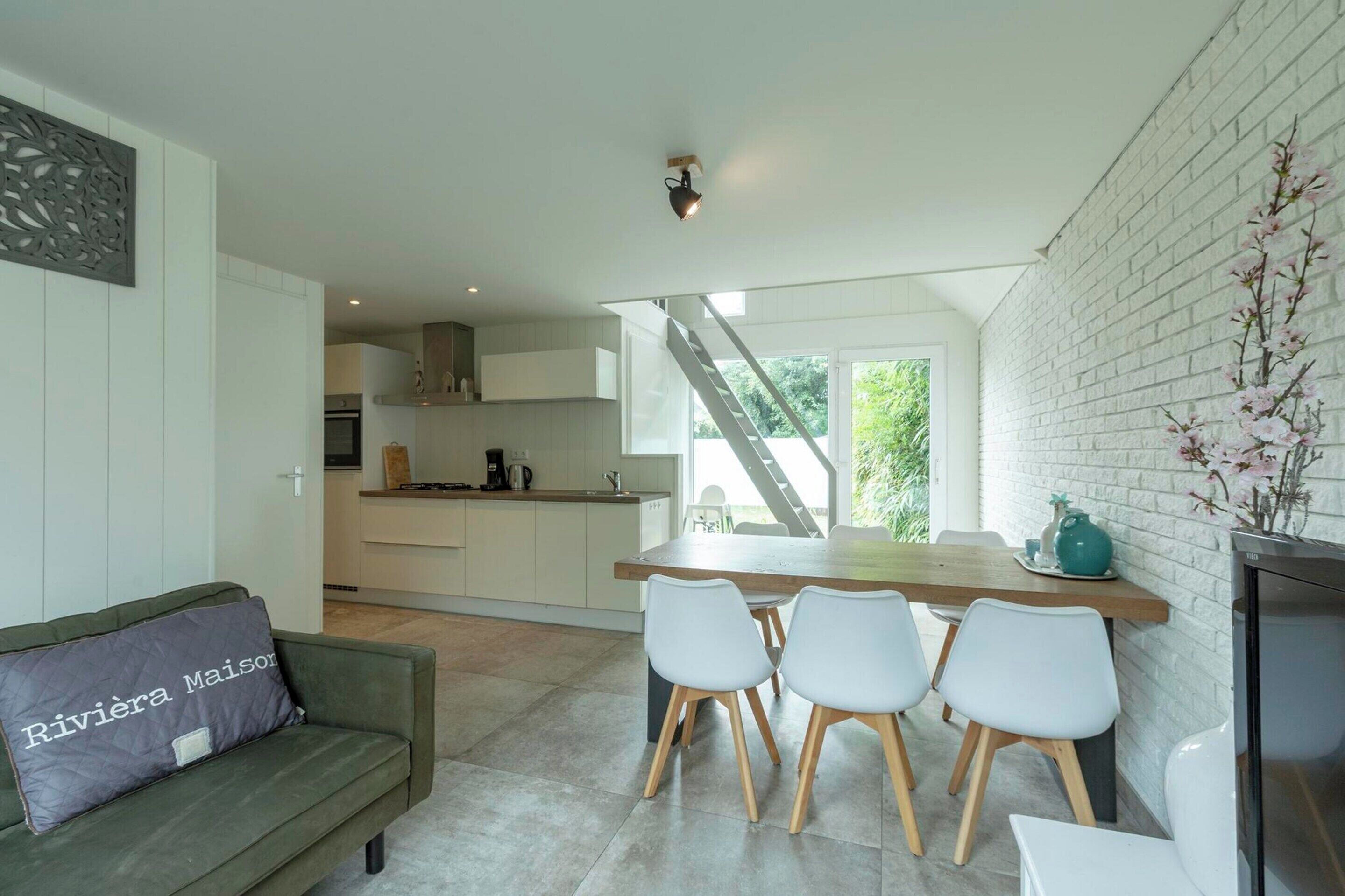 A modern kitchen with white cabinets, a wooden dining table, and a staircase leading to an upper level.
