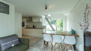 Une cuisine moderne avec des meubles blancs, une table à manger en bois et un escalier menant à l’étage supérieur.
