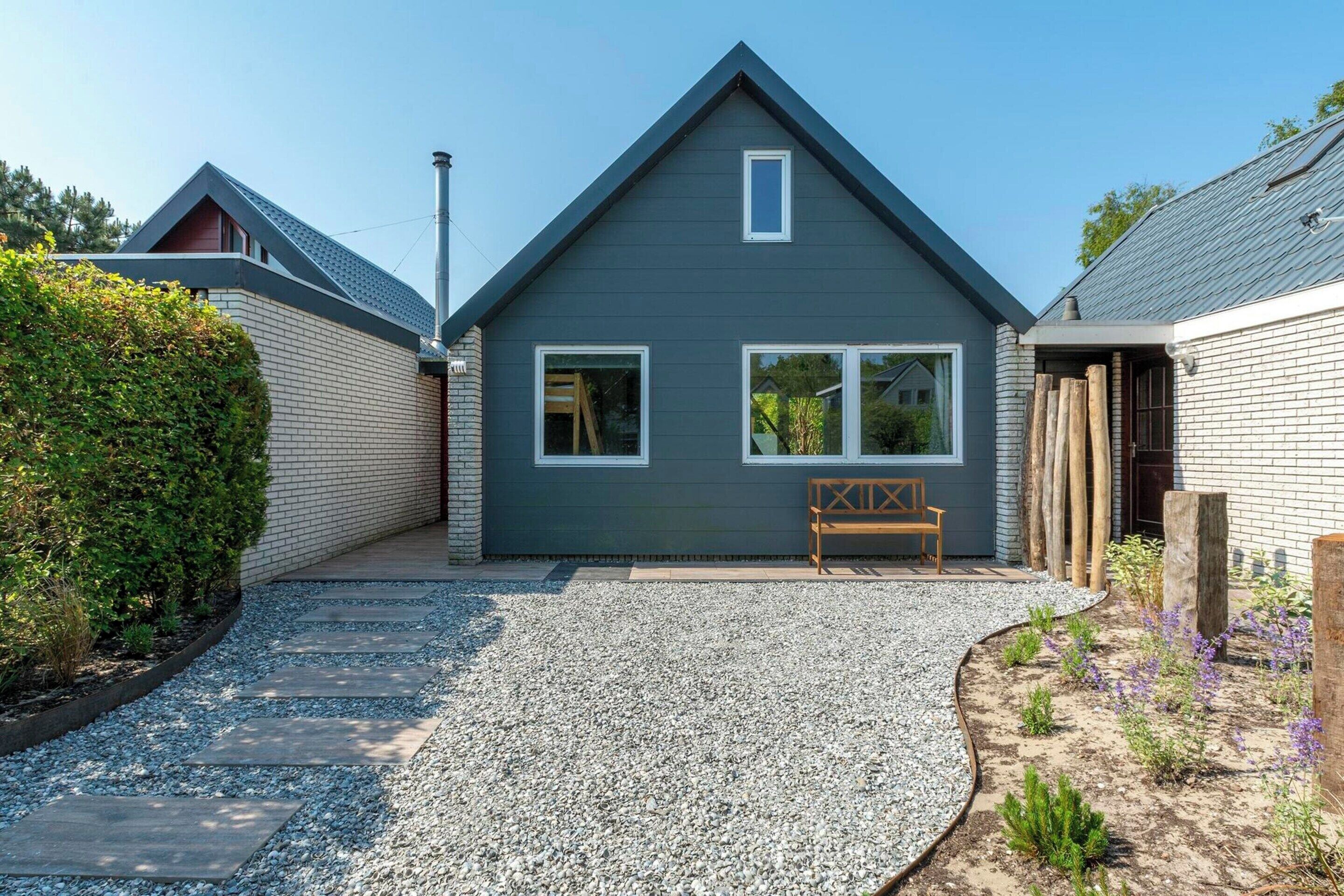 A modern house with a grey exterior, a sloped roof, and a gravel driveway.