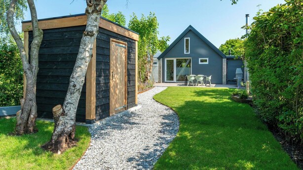 Une maison moderne avec un chemin de gravier menant à un patio aménagé avec du mobilier d’extérieur.