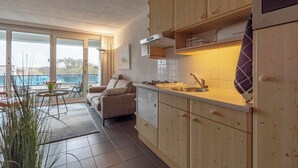 A modern kitchen with wooden cabinets, a built-in stove, and a large window overlooking a balcony. - Studio in Groote Keeten by the Beach (Callantsoog)