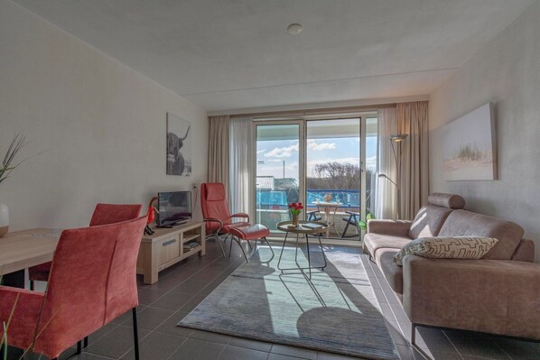 En moderne stue med spiseplads, sofa, fjernsyn og et stort vindue med udsigt.