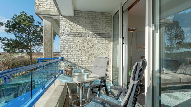 A balcony with a glass railing, a table with chairs, and a view of the interior through a glass door. - Studio in Groote Keeten by the Beach (Callantsoog)