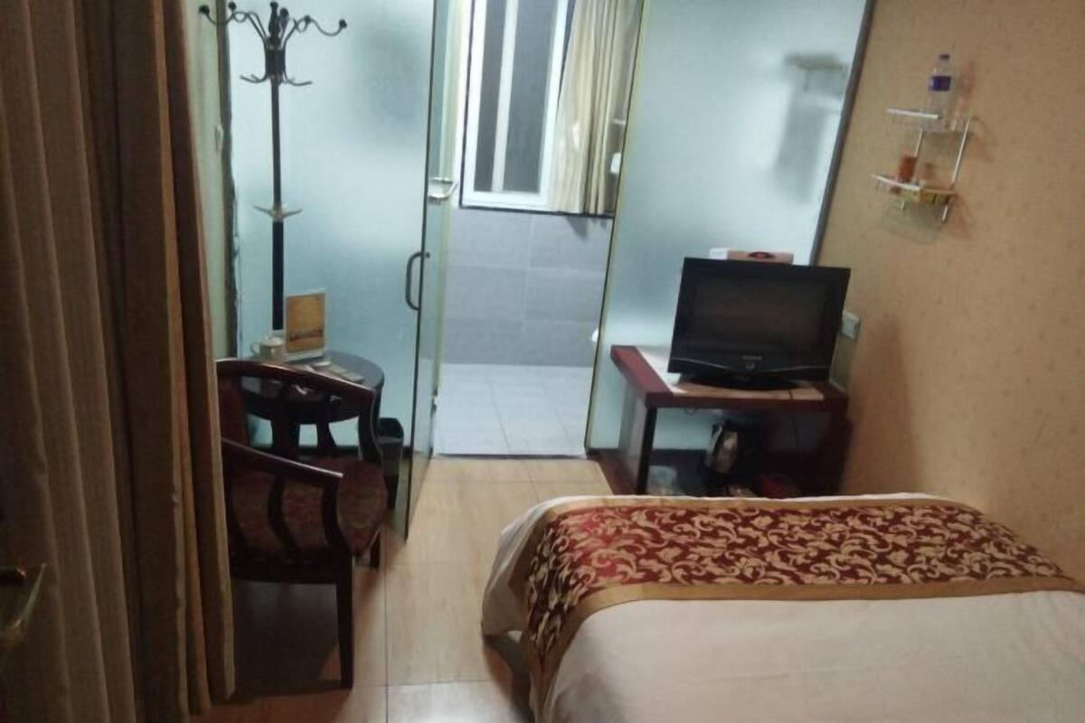 Una habitación de hotel pequeña con cama, escritorio con televisor, una silla y perchero.
