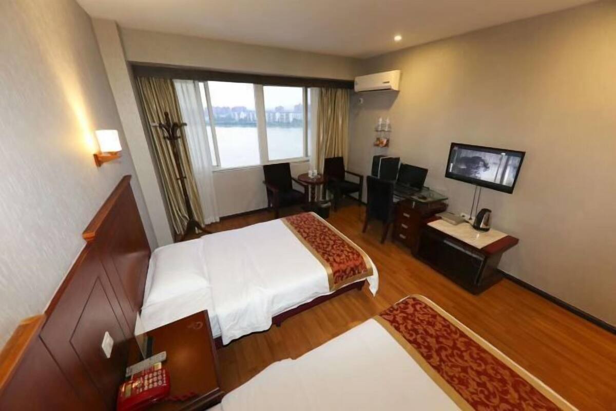 Habitación de hotel con dos camas, un escritorio, una silla, un televisor y una ventana con vista al agua.