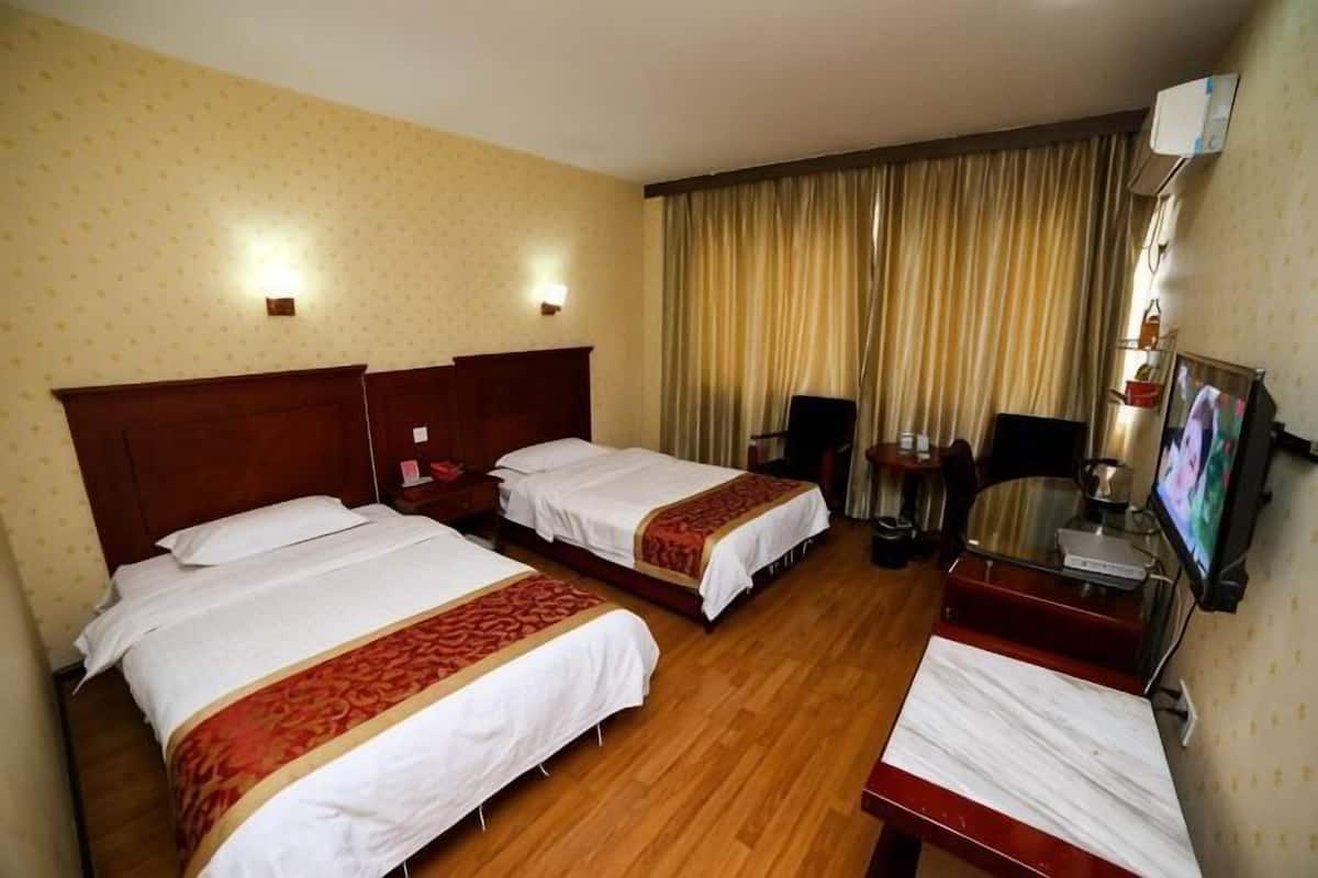 Habitación de hotel con dos camas, un escritorio, una silla, un televisor y una ventana con cortinas.