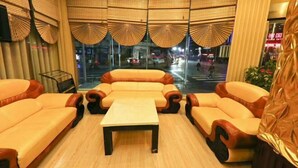 Ein Zimmer mit einer Sofagarnitur, einem kleinen Tisch und Blick auf die Straße durch große Fenster.