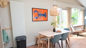 A dining area with a wooden table, blue chairs, a black trash bin, and a framed lobster picture on the wall.