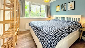 A bedroom with a bed, a wooden crib, a window with curtains, and a hanging light fixture.