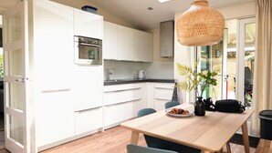 A modern kitchen with white cabinets, a wooden dining table, and a hanging light fixture.