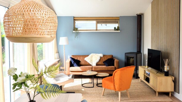 A modern living room with a sofa, coffee table, and orange chair. There is a television on a wooden stand and a large woven light fixture.