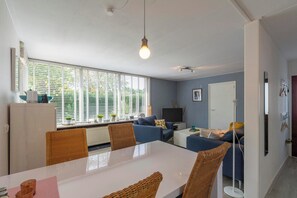 Een moderne woonkamer met een eethoek, grote ramen en een televisie.