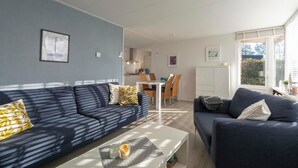 A modern living room with two dark sofas, a white coffee table, and a dining area with a white table and chairs. - Holiday Home Near Bulb Fields With Garden (Sint Maartensvlotbrug)