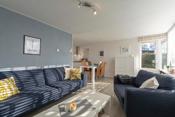 Een moderne woonkamer met twee donkere banken, een witte salontafel en een eethoek met een witte tafel en stoelen.