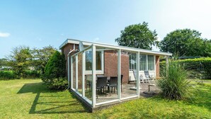 A glass-enclosed patio with a brick exterior, outdoor seating, and a view of the surrounding garden. - Holiday Home Near Bulb Fields With Garden (Sint Maartensvlotbrug)