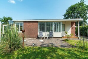 Een modern huis met een bakstenen gevel, grote ramen en een terras met twee stoelen en een tafel.