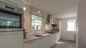 A modern kitchen with white cabinets, a stainless steel oven, a sink, and a window providing natural light. - Holiday Home Near Bulb Fields With Garden (Sint Maartensvlotbrug)