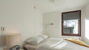 A bedroom with a bed, a bedside table with a lamp, a window with a view, and a radiator. - Holiday Home Near Bulb Fields With Garden (Sint Maartensvlotbrug)