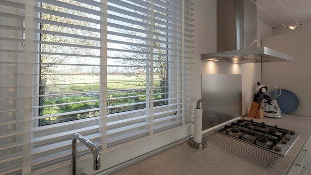A modern kitchen with a gas stove, a stainless steel range hood, and a window with white blinds. - Holiday Home Near Bulb Fields With Garden (Sint Maartensvlotbrug)