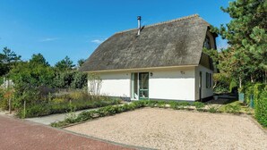 A single-story house with a thatched roof, a gravel driveway, and a small garden area. - Duynopgangh 16 Villa for 8-guests Behind Dunes (Julianadorp)