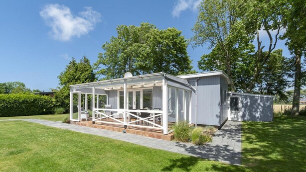 A modern outdoor patio area with a glass enclosure, a small shed, and a well-maintained lawn. - Modern Holiday Home With Large Garden (Sint Maartensvlotbrug)