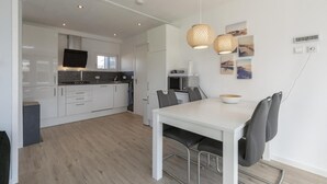 A modern kitchen with white cabinets, a dining table with chairs, and a large window. - Modern Holiday Home With Large Garden (Sint Maartensvlotbrug)
