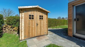 A wooden shed with two windows and a door, adjacent to a building with a large window and a screen door. - Bungalow in Julianadorp Near Sandy Beach (Julianadorp)