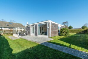 A modern house with a patio, a glass door leading to a covered outdoor area, and a well-maintained lawn.