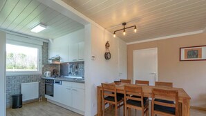 A kitchen with white cabinets, a stove, and a sink. There is a dining table with chairs. - Bungalow in Julianadorp Near Sandy Beach (Julianadorp)