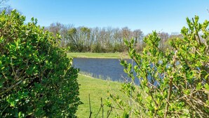A serene lakeside view with dense greenery and trees in the background. - Bungalow in Julianadorp Near Sandy Beach (Julianadorp)