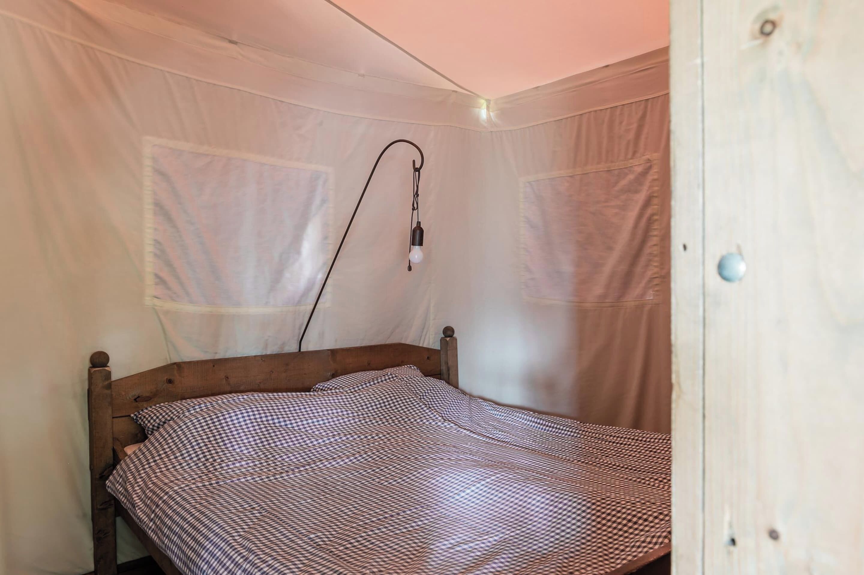 A single bed with a checkered bedspread in a room with white walls and a wooden door.