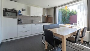 A modern kitchen with white cabinets, a built-in oven, and a dining area with a wooden table and black chairs.