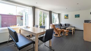 A modern living room with a dining area, large windows, and a view of a building outside.