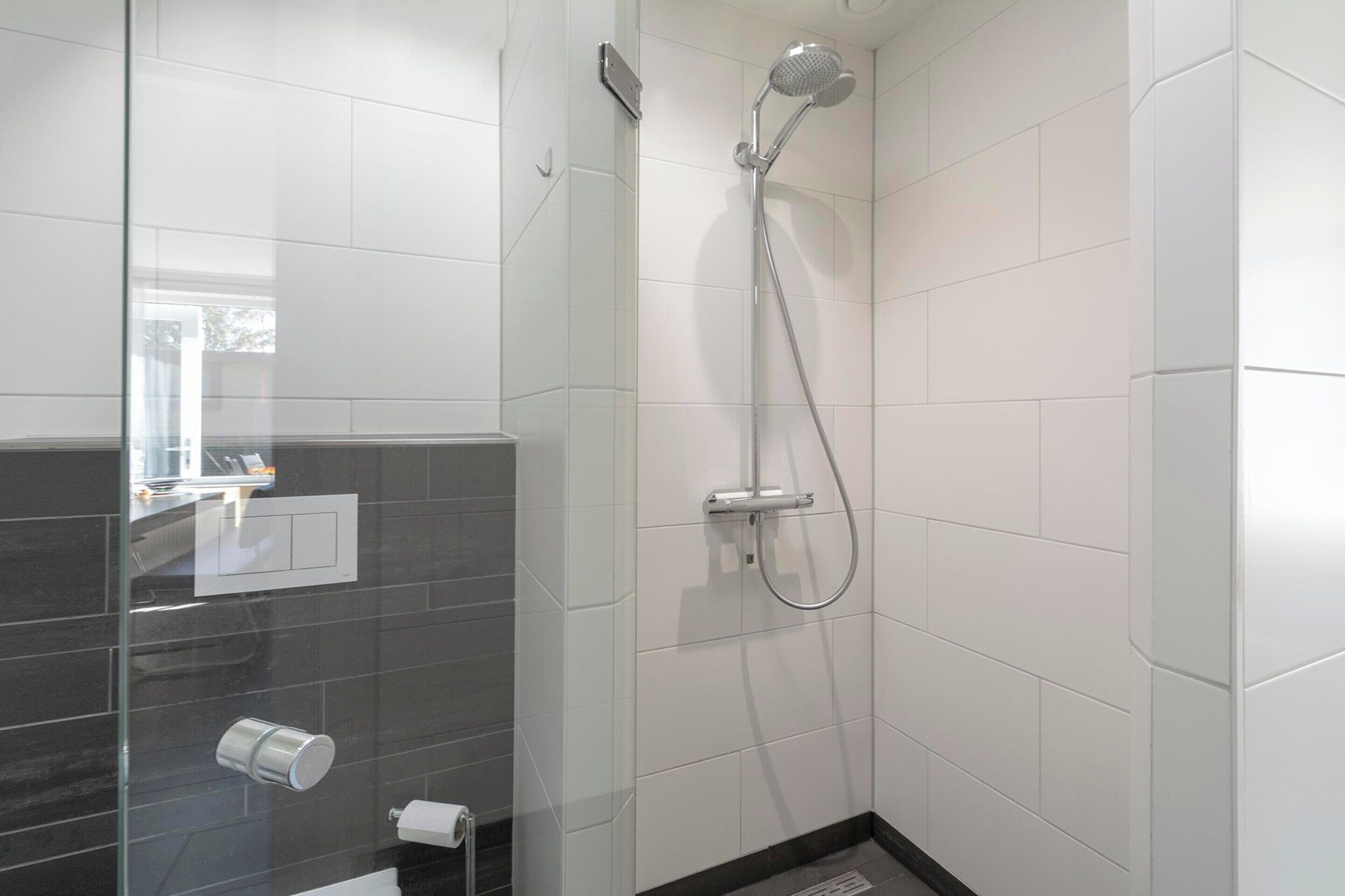 A modern bathroom with a glass shower enclosure, white tiled walls, and a black-tiled accent wall.