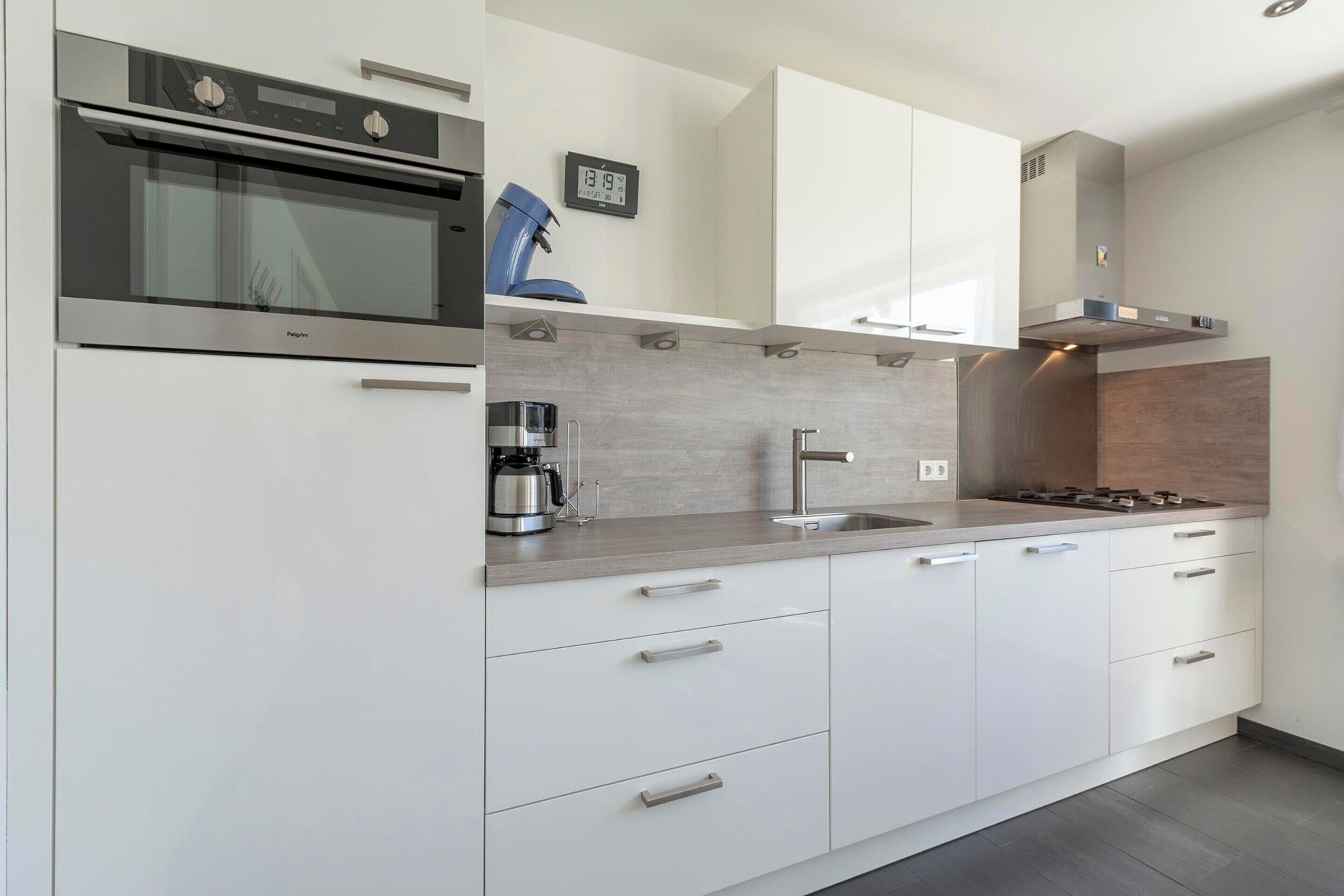 A modern kitchen with white cabinets, stainless steel appliances, a coffee maker, and a clock on the wall.