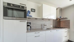 A modern kitchen with white cabinets, stainless steel appliances, a coffee maker, and a clock on the wall.