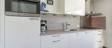 A modern kitchen with white cabinets, stainless steel appliances, a coffee maker, and a clock on the wall.