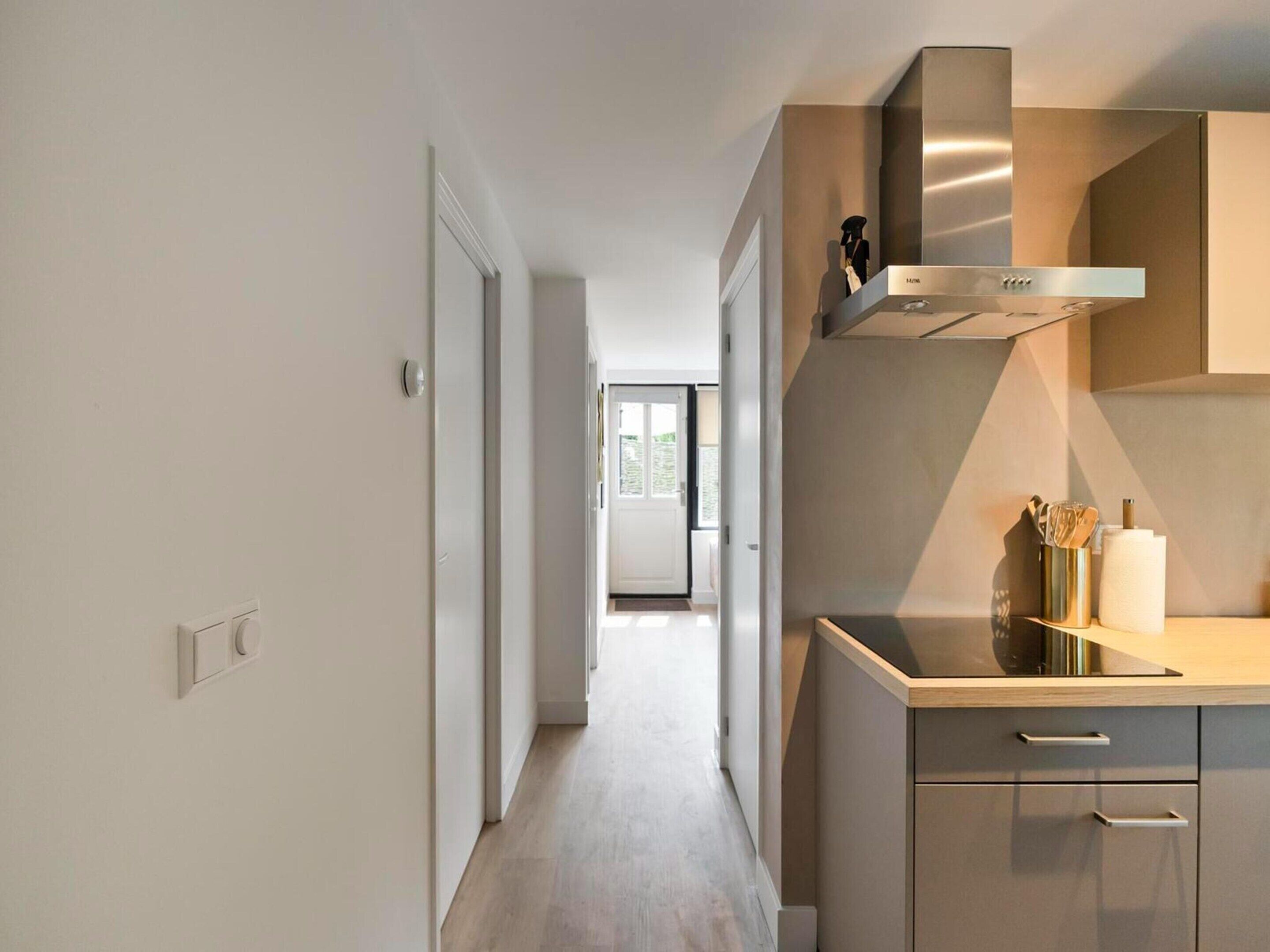 A modern kitchen with a stainless steel range hood, a countertop with a vase of flowers, and a view into the adjacent living area.