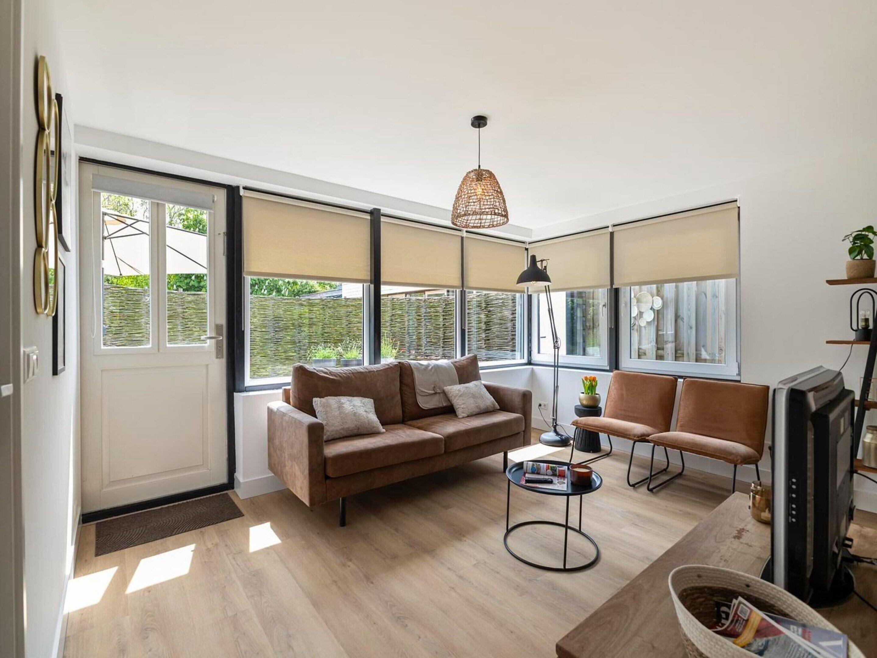 Una sala de estar moderna con un sofá, un sillón y una mesa de centro. Hay un televisor y una lámpara.