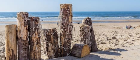 Een houten strandbarrière met touwen, een zandstrand en de oceaan op de achtergrond.