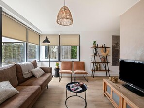 A modern living room with a sofa, chairs, a coffee table, a TV, and a bookshelf. - Bungalow in Sint Maartenszee Near Sandy Beach (Sint Maartensvlotbrug)