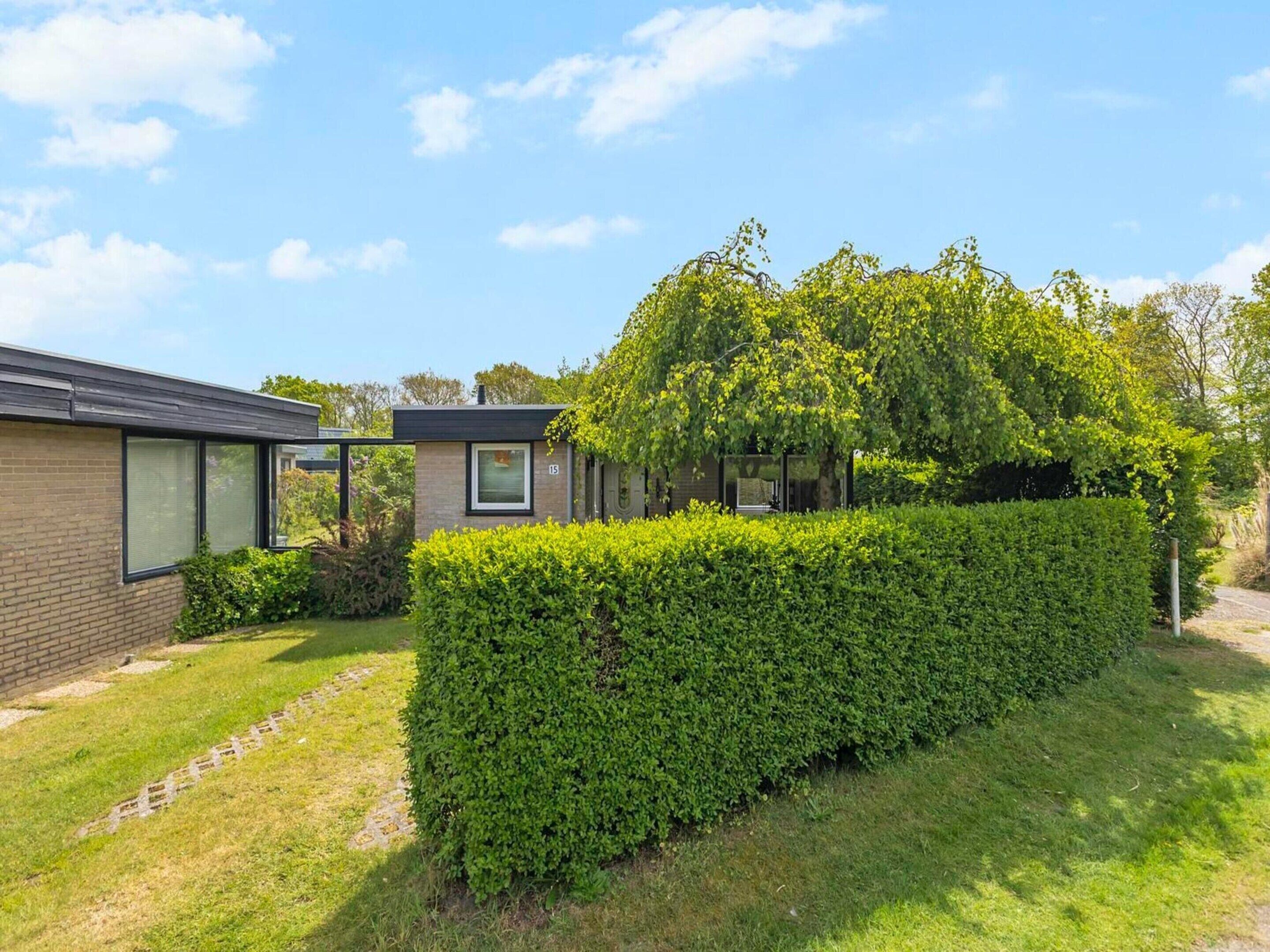 A modern house with a brick exterior, a glass conservatory, and a well-maintained hedge.