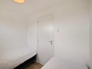 A small, single-room accommodation with two single beds, a white door, and a light switch on the wall. - Bungalow in Sint Maartenszee Near Sandy Beach (Sint Maartensvlotbrug)