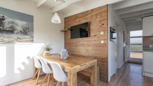 A modern kitchen with a wooden wall, a dining table with chairs, and a TV mounted above it. - Duinland 247modern Bungalow for 6 Guests (Sint Maartensvlotbrug)