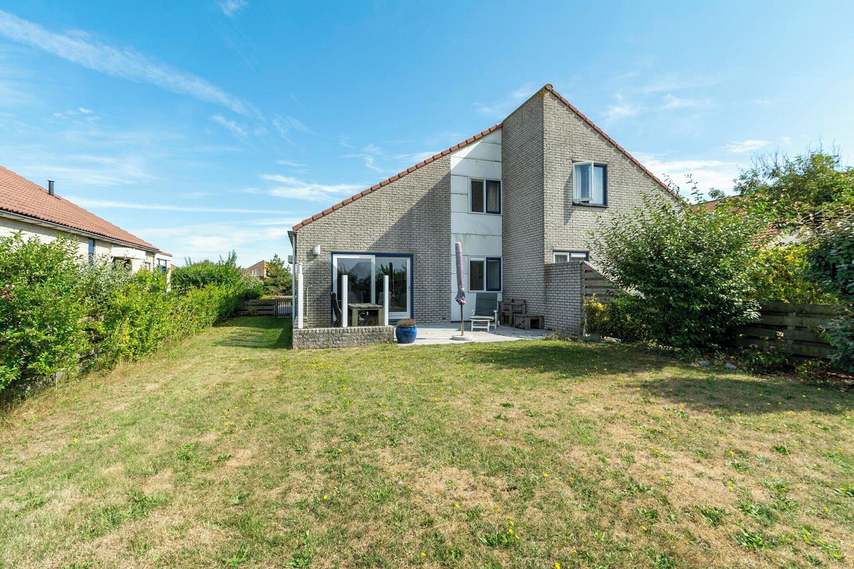 A modern two-story house with a sloped roof, a patio with outdoor furniture, and a well-maintained lawn.